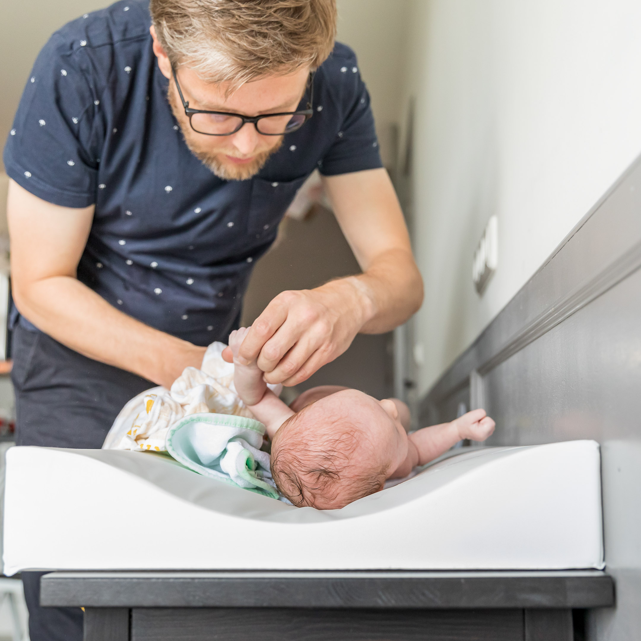 Newborn fotografie; papa kleedt baby aan tijdens lifestyleshoot Uithuizen